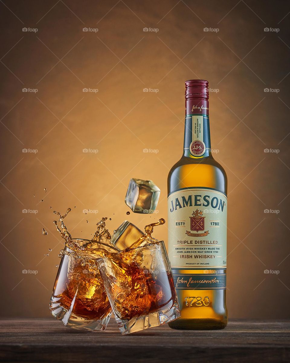 A bottle of Jameson whiskey.  Glasses with whiskey and falling ice cubes and splashes