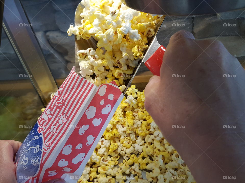 Hands pouring fresh popcorns into carton