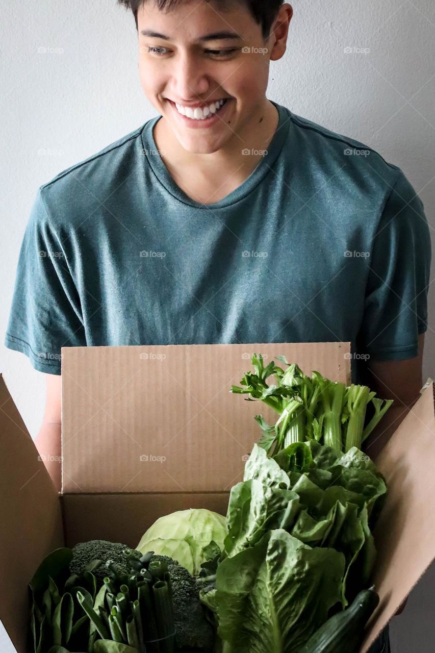 Handsome young man is holding a cardboard box with green vegetables