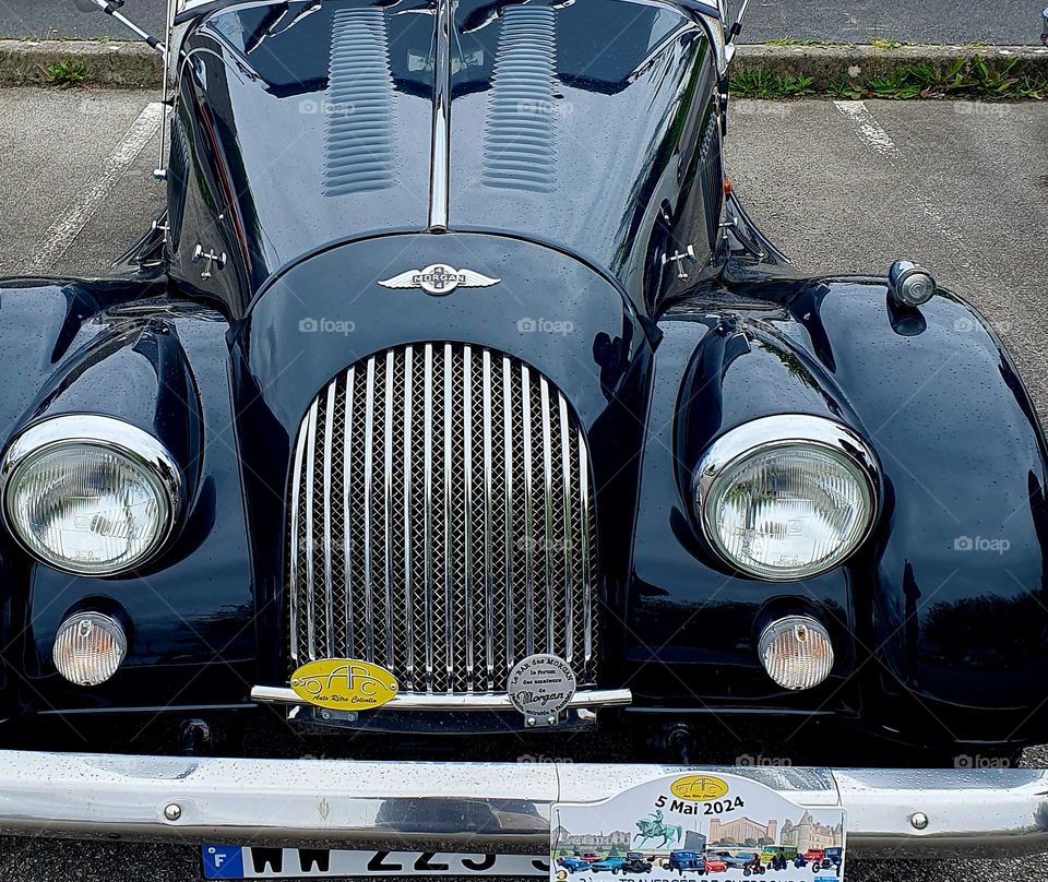 The front of a dark green Morgan Convertible showing the grill and lights at Cherbourg car show