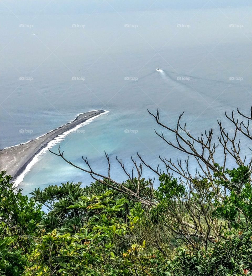 A prominent beach of an island, has a beautiful coastline with a ship in the blue sea. we climb high and gaze far!