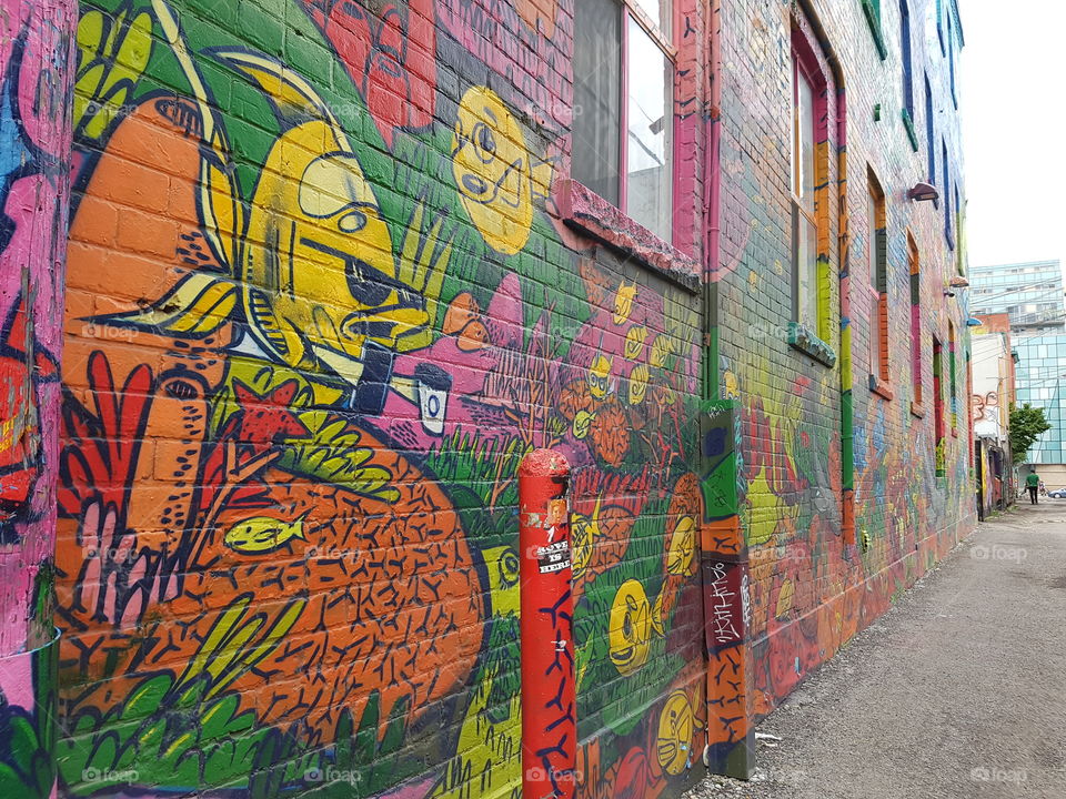 Brightly coloured graffiti alley in downtown Toronto, Ontario. Green, yellow, and orange spray paints lights up the walls of our city.