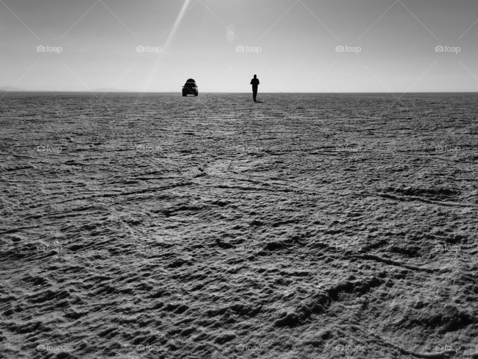 A man alone with his car on salt flats in Salar de Uyuni, Bolivia