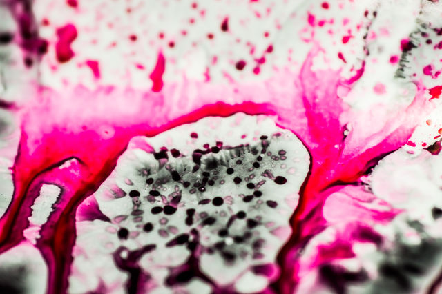 Black and pink refill ink spilled onto the white sink and the ink mixed into abstract blobs and patterns.