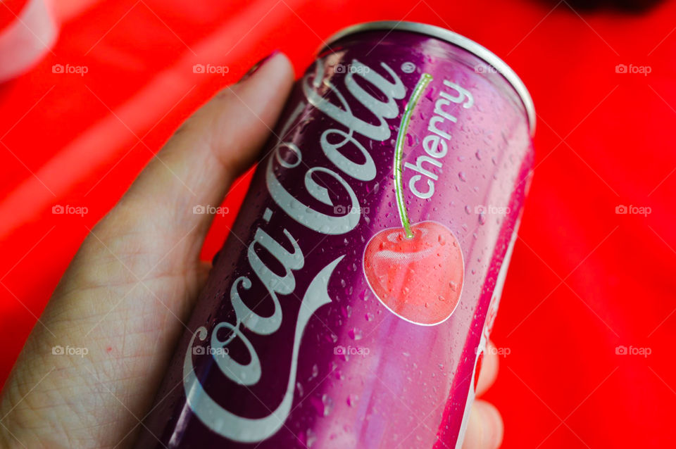 A person’s hand holding a can of cherry Coke a cola with a red