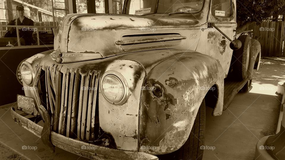 An old vintage Fird truck forever waits for an attendant to check under the hood. The attendant is actually a mannequin on display in a city landmark gas station placed in a history park.