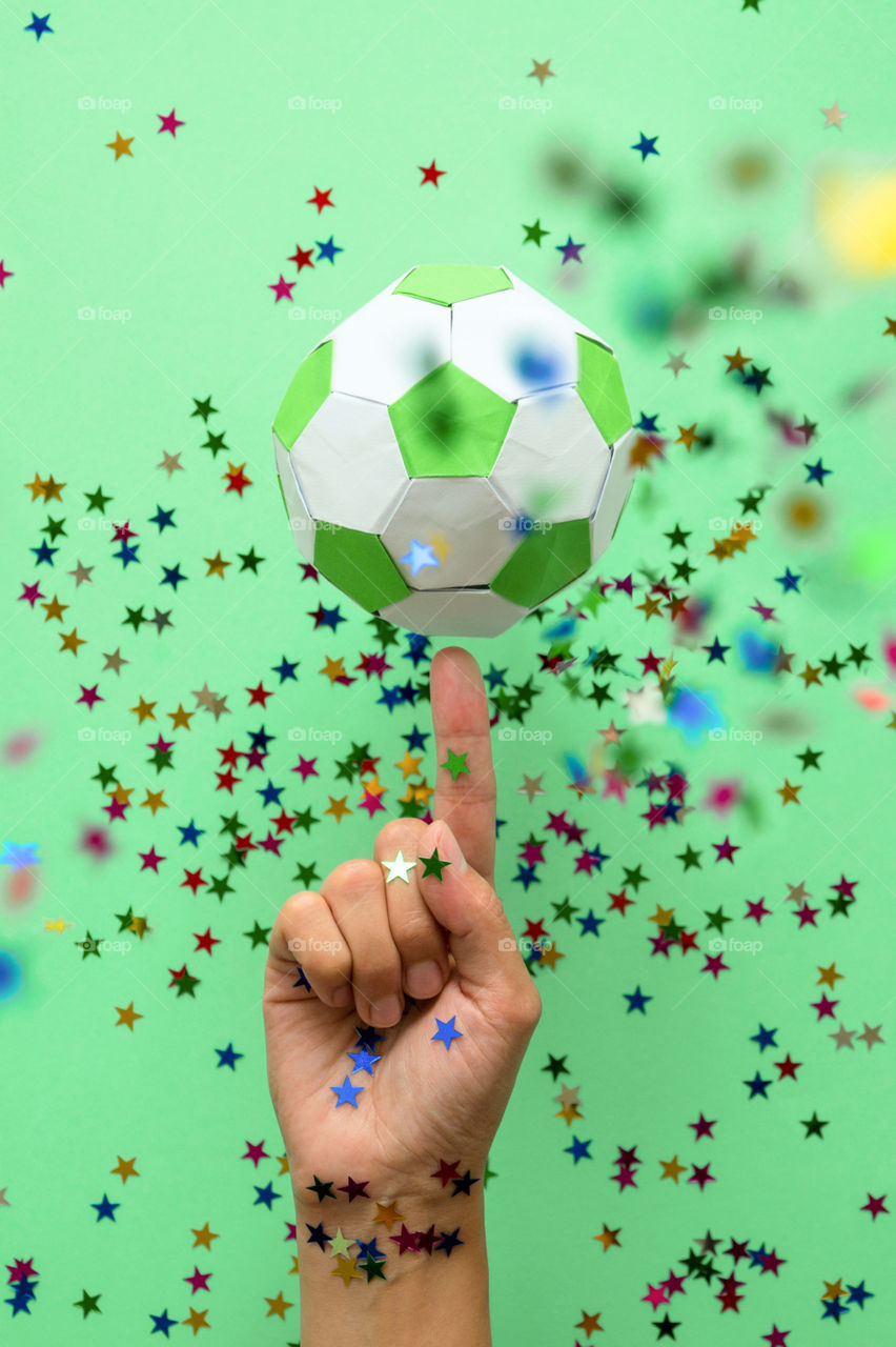 Hand spinning paper soccer ball on green background. Origami. Paper craft. Soccer game concept.