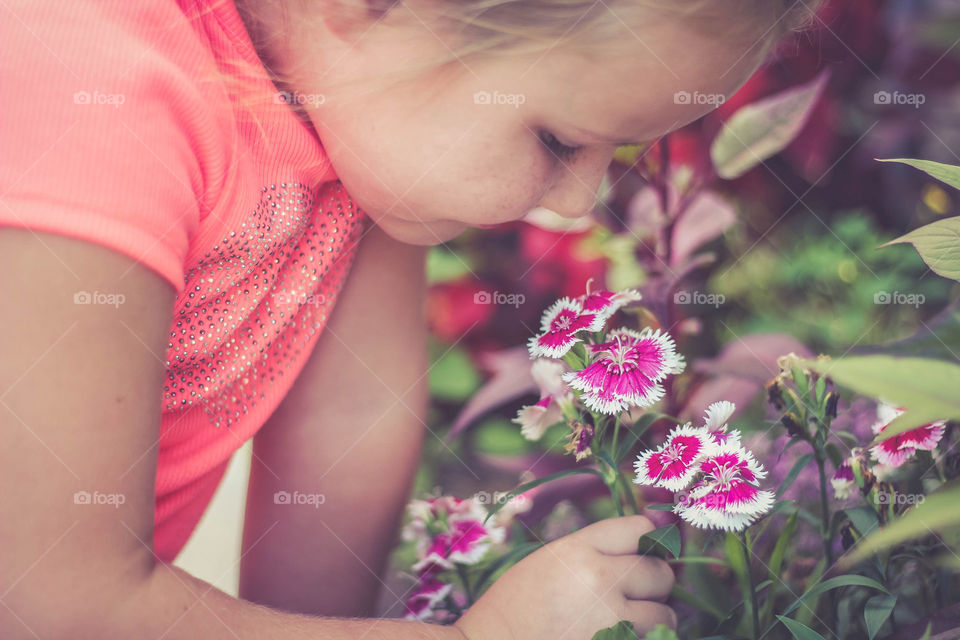Little girl in pink shirt smelling pink spring flowers 