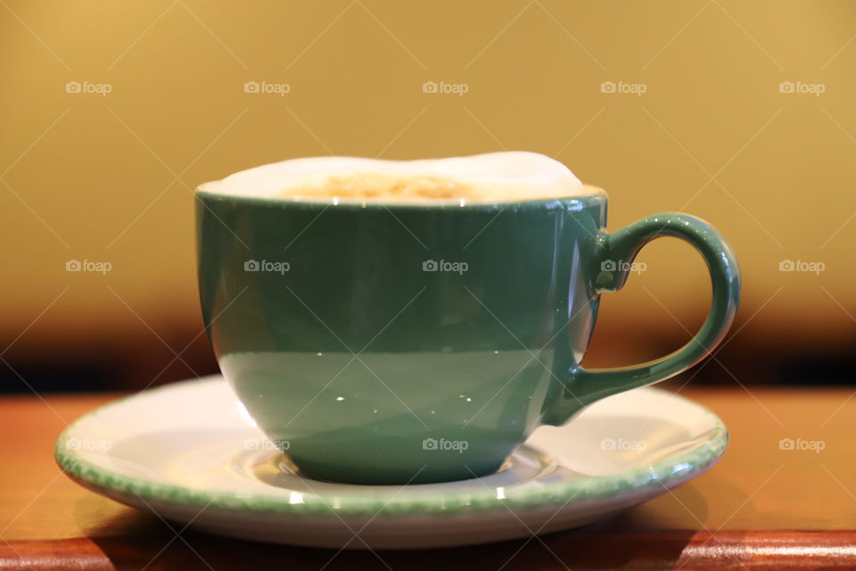 Green cup of cappuccino on top of white saucer laying on the countertop against the wall