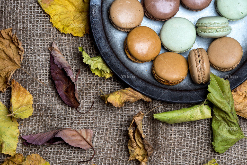 rustic plate with macaroons on natural fabric texture, sourranded with autumn leaves, top view