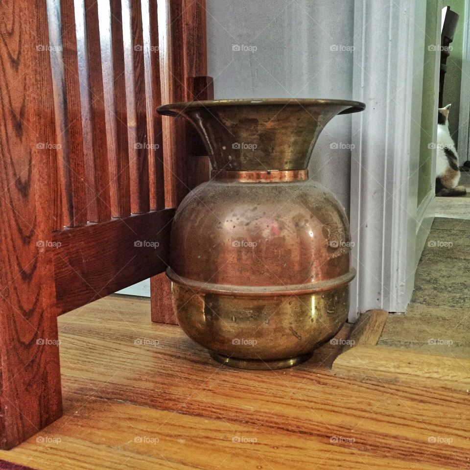 A brass spittoon sits next to a desk and a doorway. The spittoon is shiny and beautifully made.
