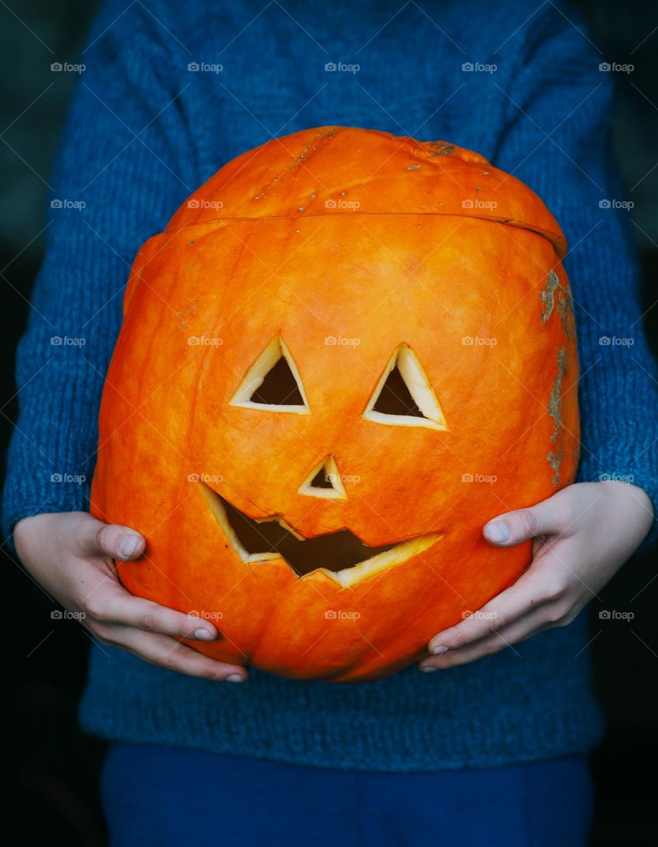 Unrecognisable boy wearing blue knitted sweater holding Halloween pumpkin 