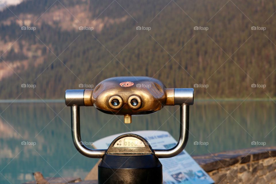 Vintage brass tourist viewing Binoculars at Lake Louise in Canada's Rocky Mountains in Banff National Park, Alberta, Canada, lake and mountains in background, 