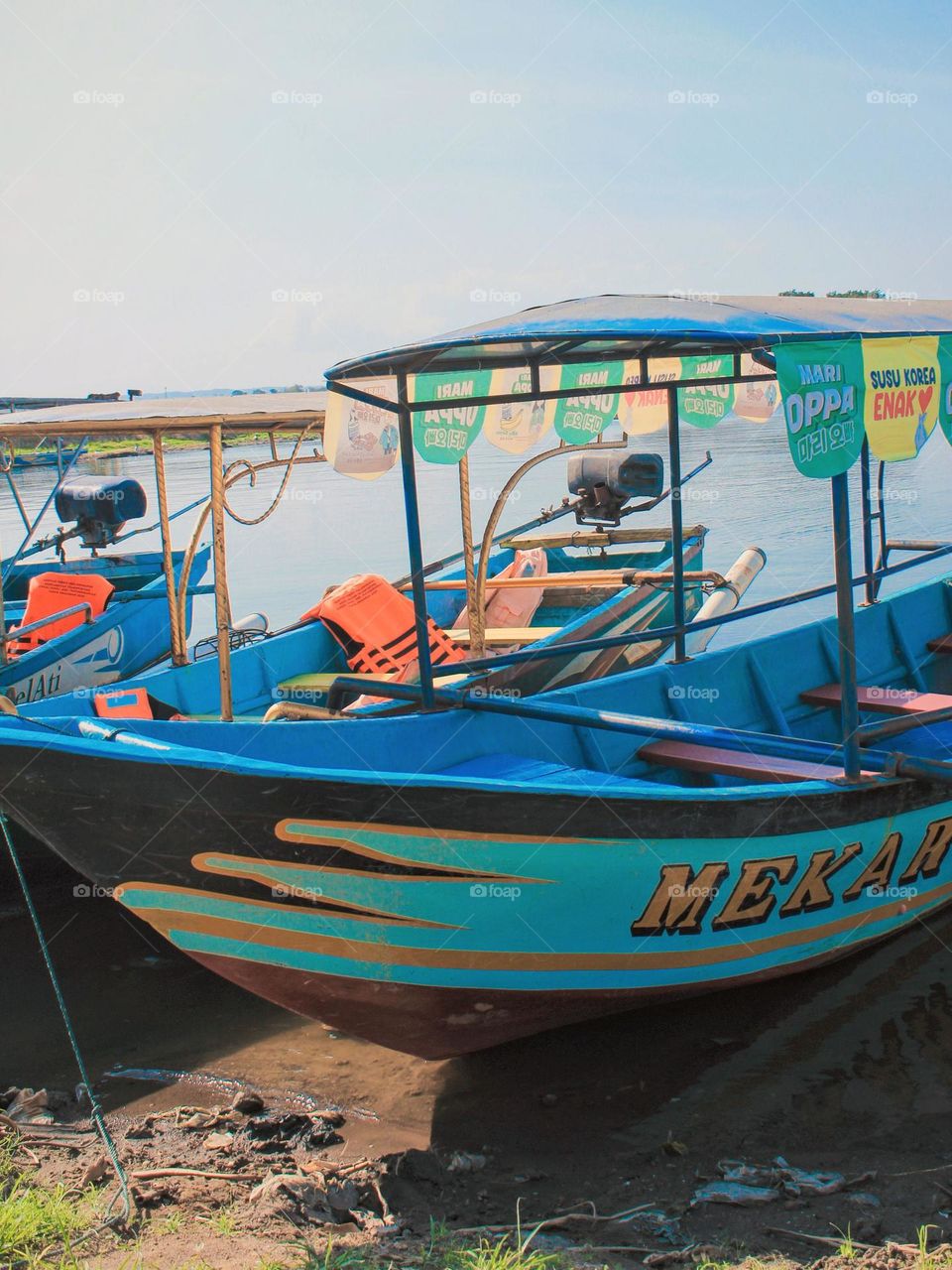 Close-up of a blue and orange boat stranded on the water's edge, with several advertising banners hanging from its roof