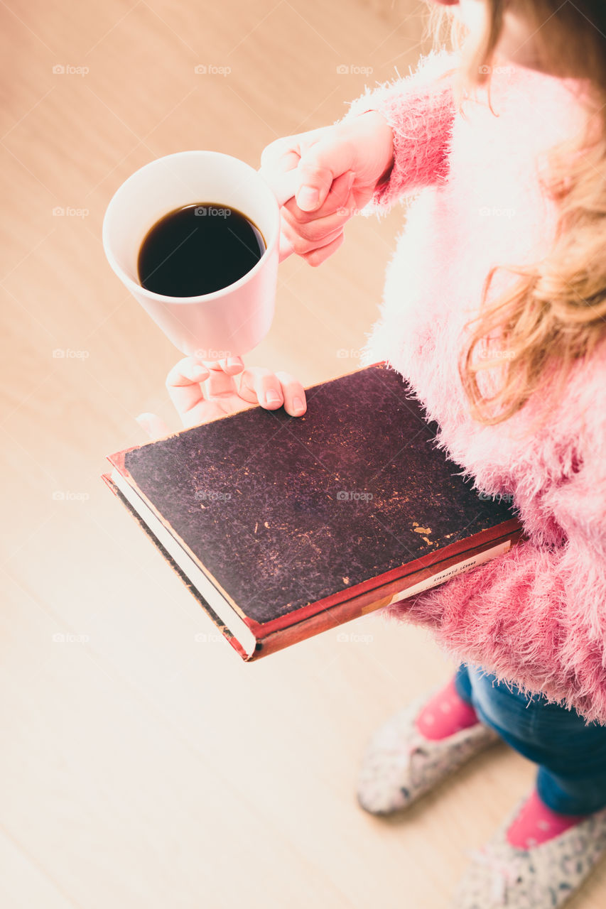 Enjoying the reading a book. Young girl holding book and cup of coffee going to relax with book. View from top