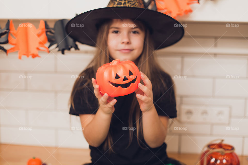 Little girl dressed as a witch for halloween holding a pumpkin with a face on the background decor