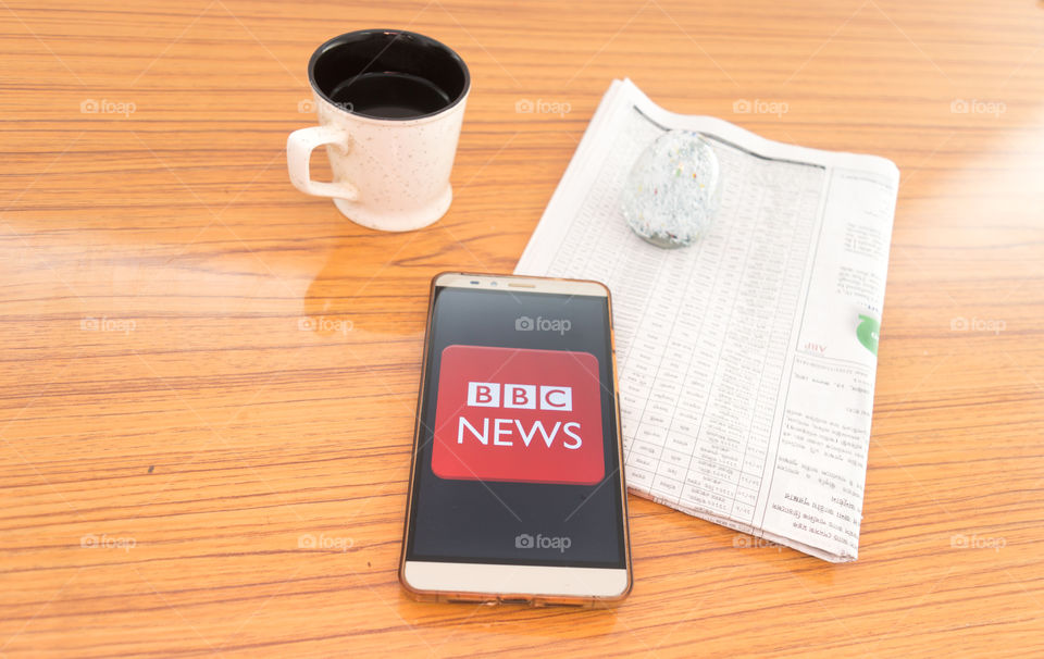 Kolkata, India, February 3, 2019: BBC news app (application) visible on mobile phone screen beautifully placed over a wooden table with a newspaper and a cup of coffee. A Technology Product Shoot.
