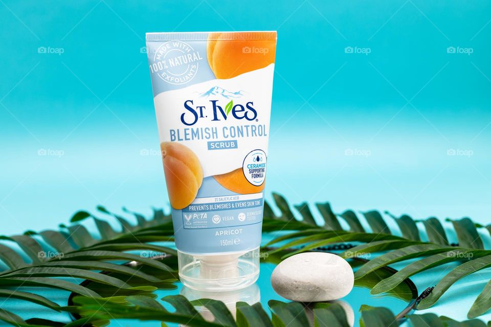 One tube of st. Ives with one stone and palm branches stands on a round mirror on a blue background, close-up view from below. Concept female cosmetics, body care, beauty.