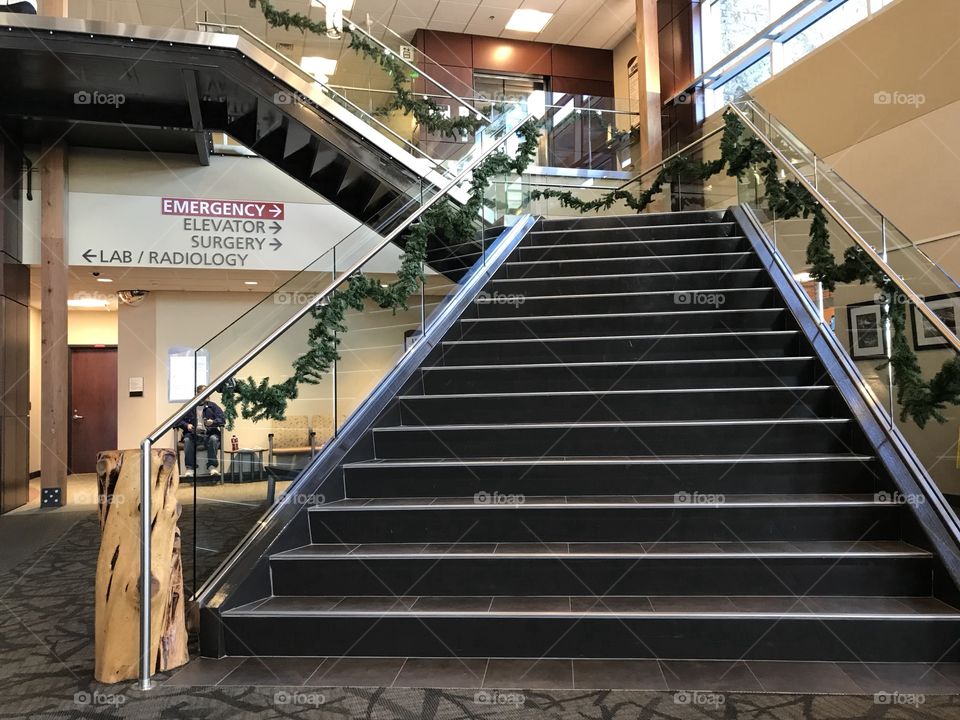 A two level stairway decorated with garland for the holiday season leads to an upper floor of a building. 