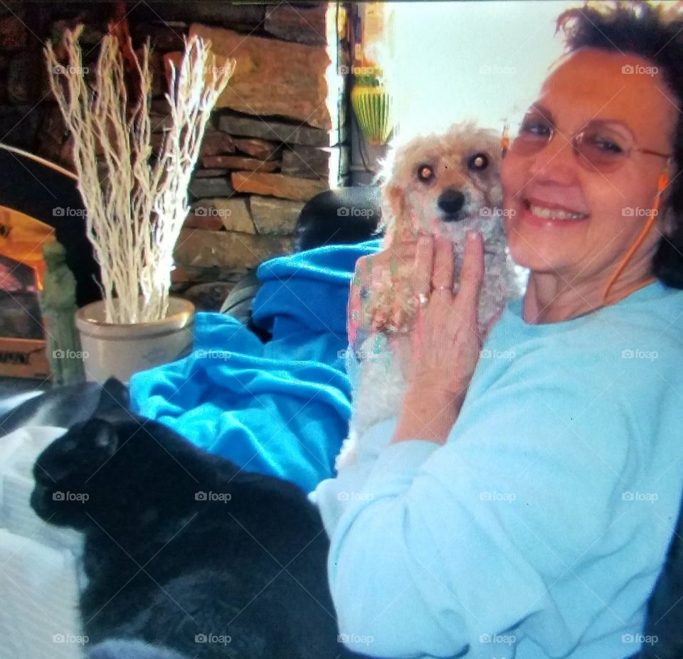 Woman on couch holding poodle, black cat on lap.