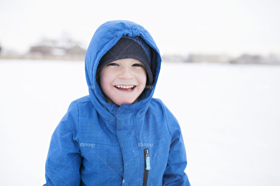 Boy in a winter coat smiling and playing in the snow 