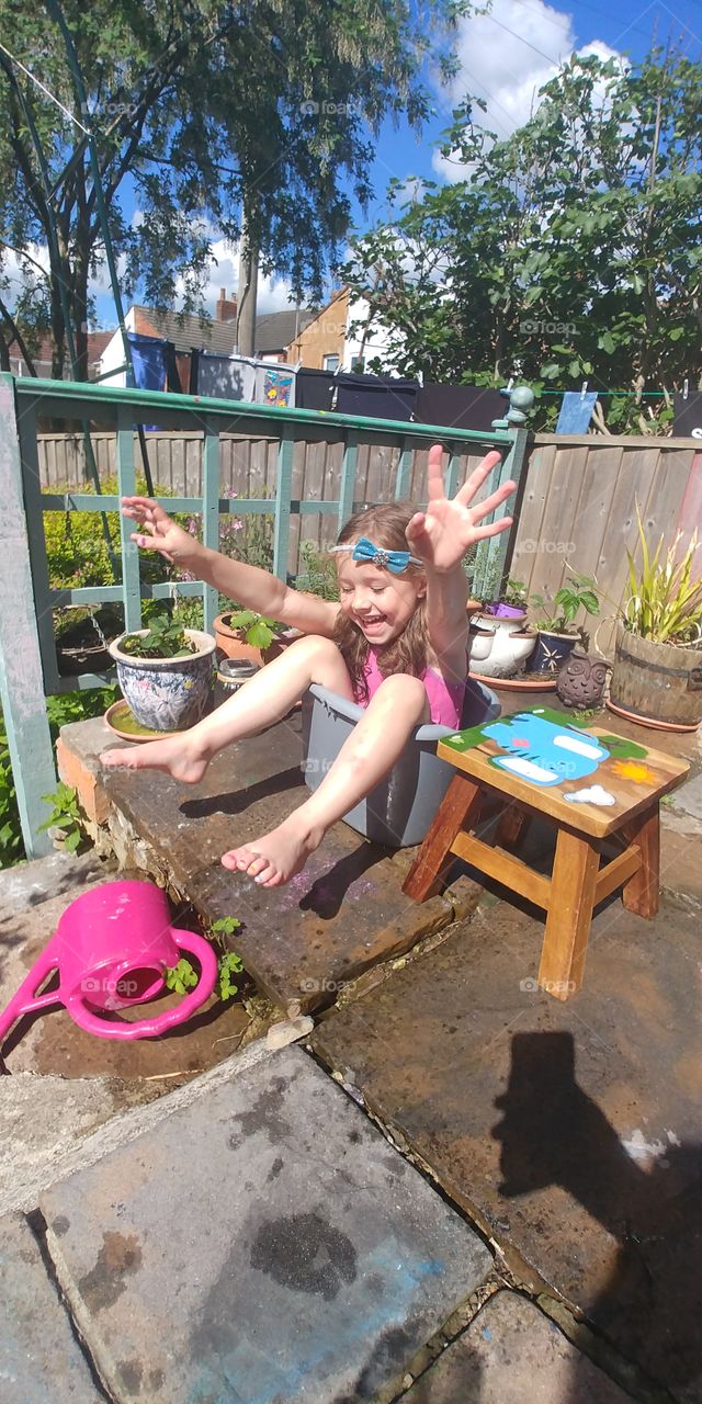 little girl playing in water bucket in bright sunshine arms raised smiling