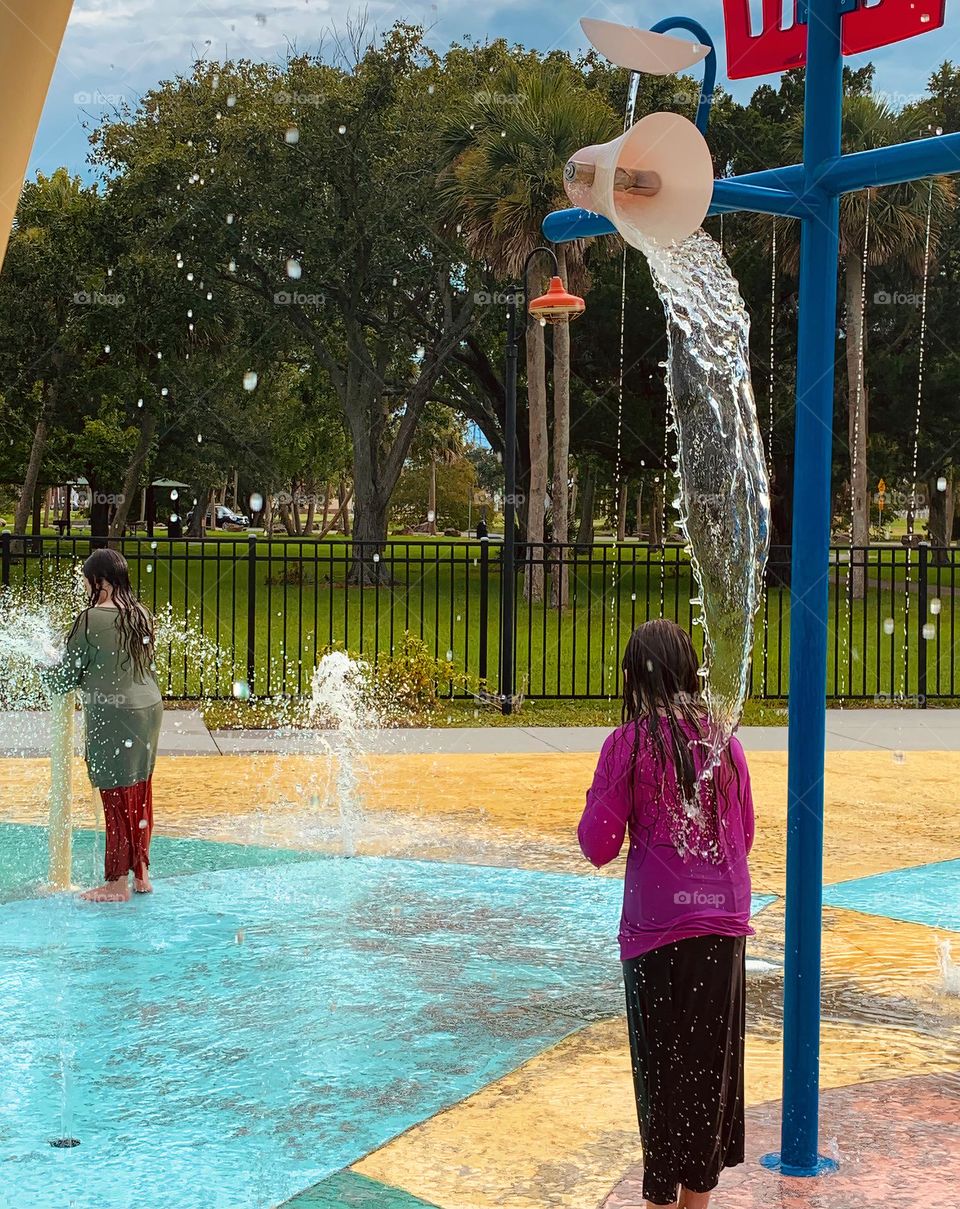 Children having lots of fun in the water at the colorful kids splash pad at the city park for children during a really warm day in Florida.