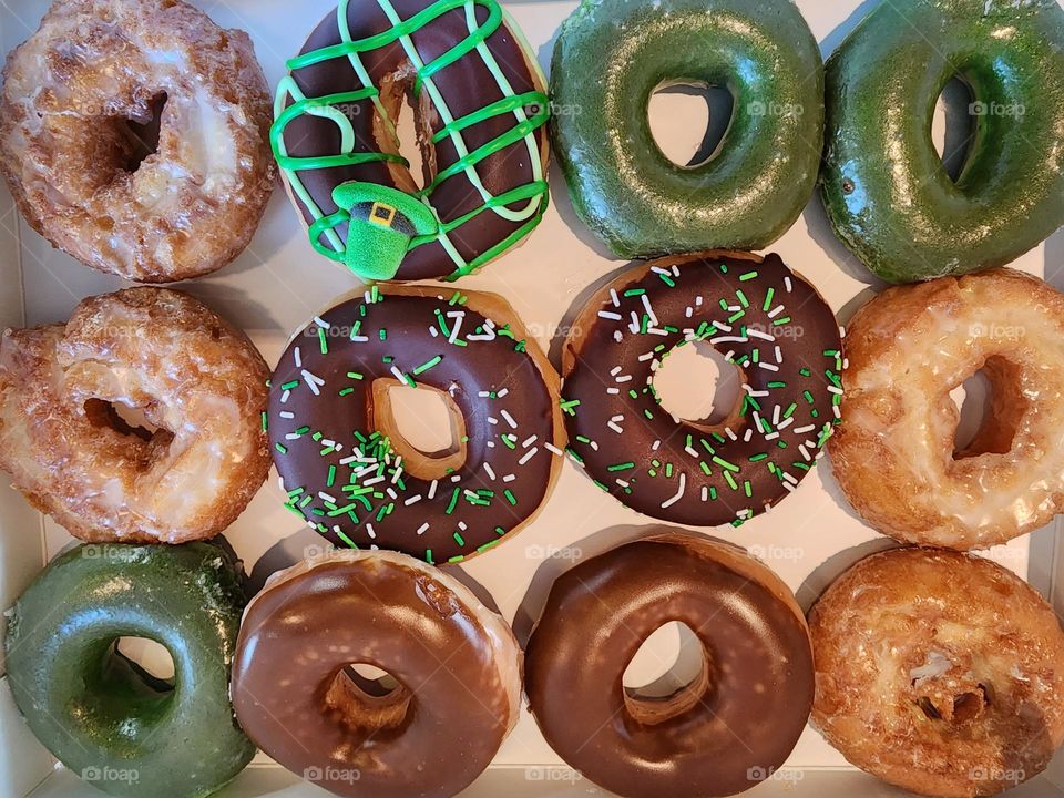 A dozen donuts of various flavors and colors fill a box that is headed for some lucky recipients