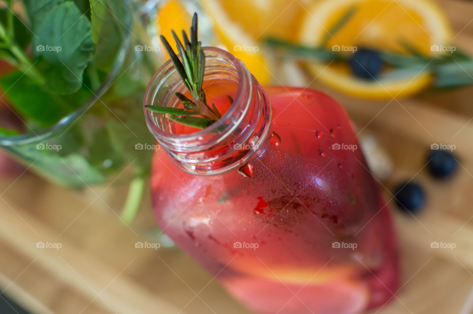 Bright colorful homemade detox drinks and flavored water on wood table made from orange juice, berry, fresh garden herbs with mint, rosemary, blueberry, ginger, orange and lemon ingredients 