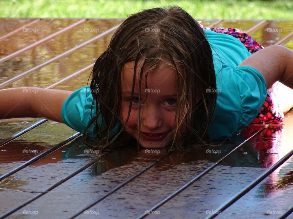 young girl enjoying water play in the backyard laying on the deck soaking wet
