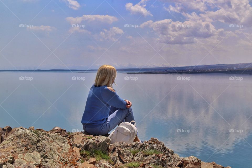 young woman sitting on the shore of a beautiful lake