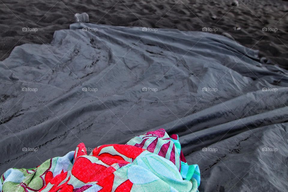 Close-up of a colorful and black blanket lying on a black sand beach