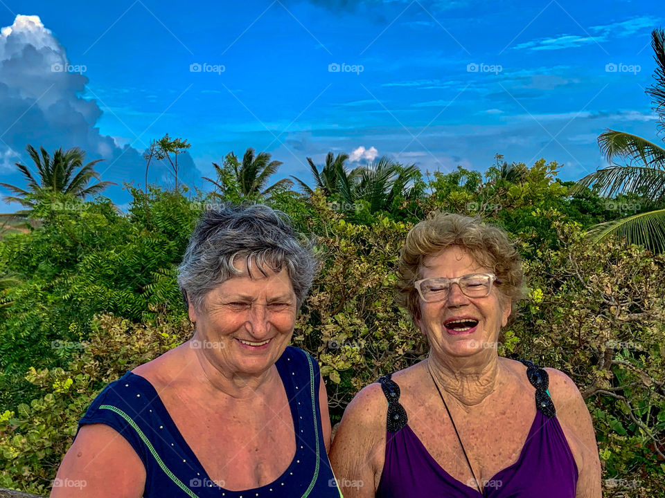 Two mature women sisters against palm trees and blue sky 
