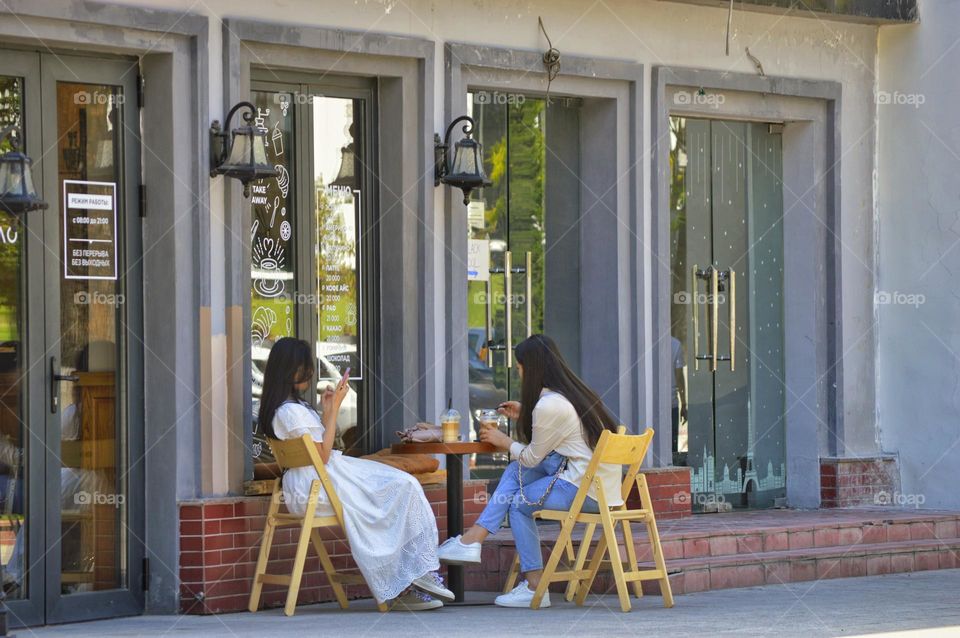 two girls drink coffee outdoors in a summer cafe