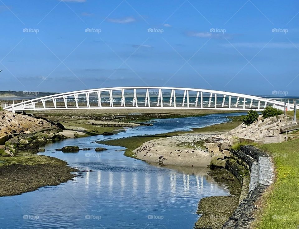 A white footbridge stand like a sentry over a tidal river flowing out to the Irish Sea in Newcastle, Northern Ireland.