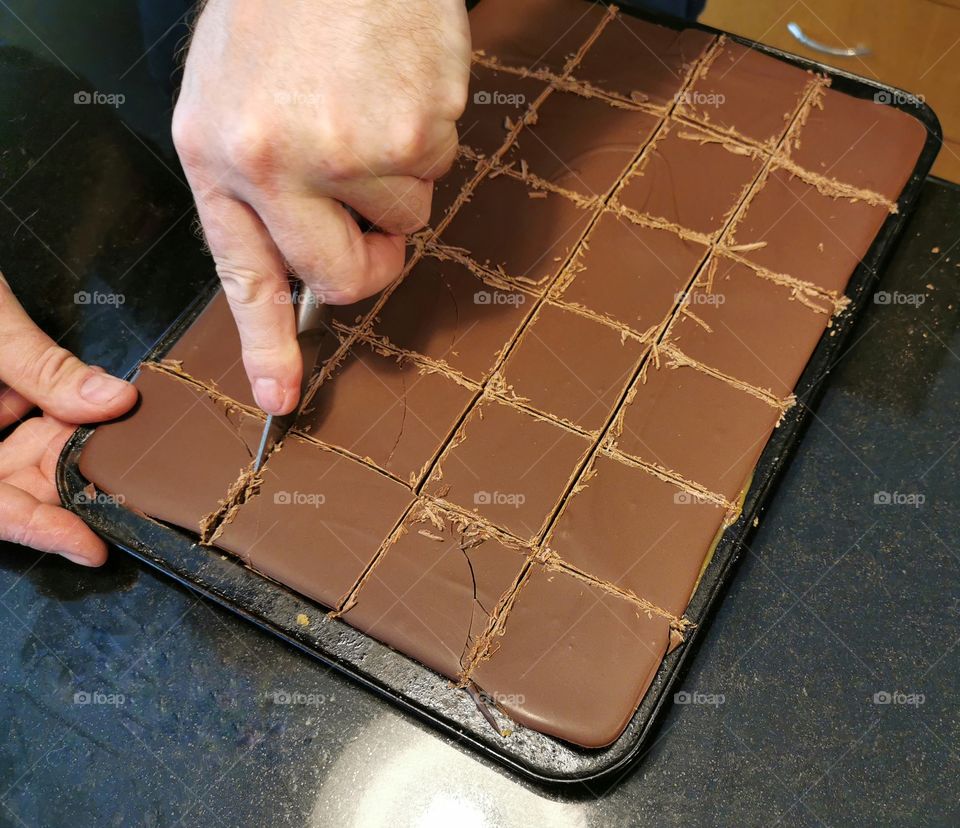 A man cutting millionaire's shortbread in the oven tray.