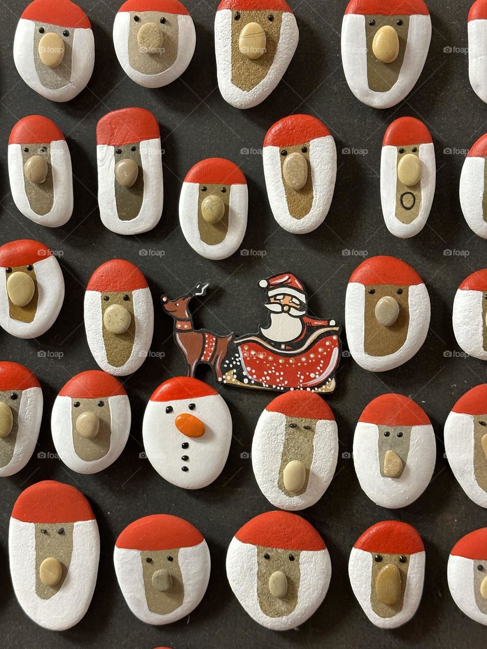 Many handmade and hand painted stone Santa Claus magnets on a wooden board 