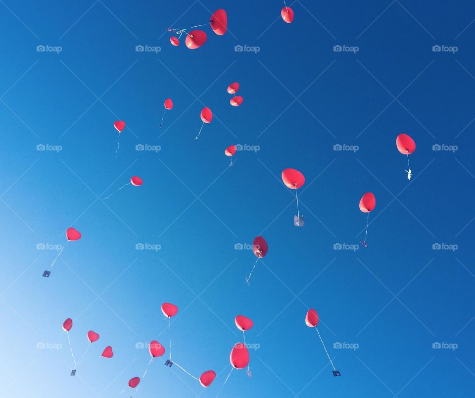 Heart-shaped helium balloons flying into the blue sky with a message attached to them.