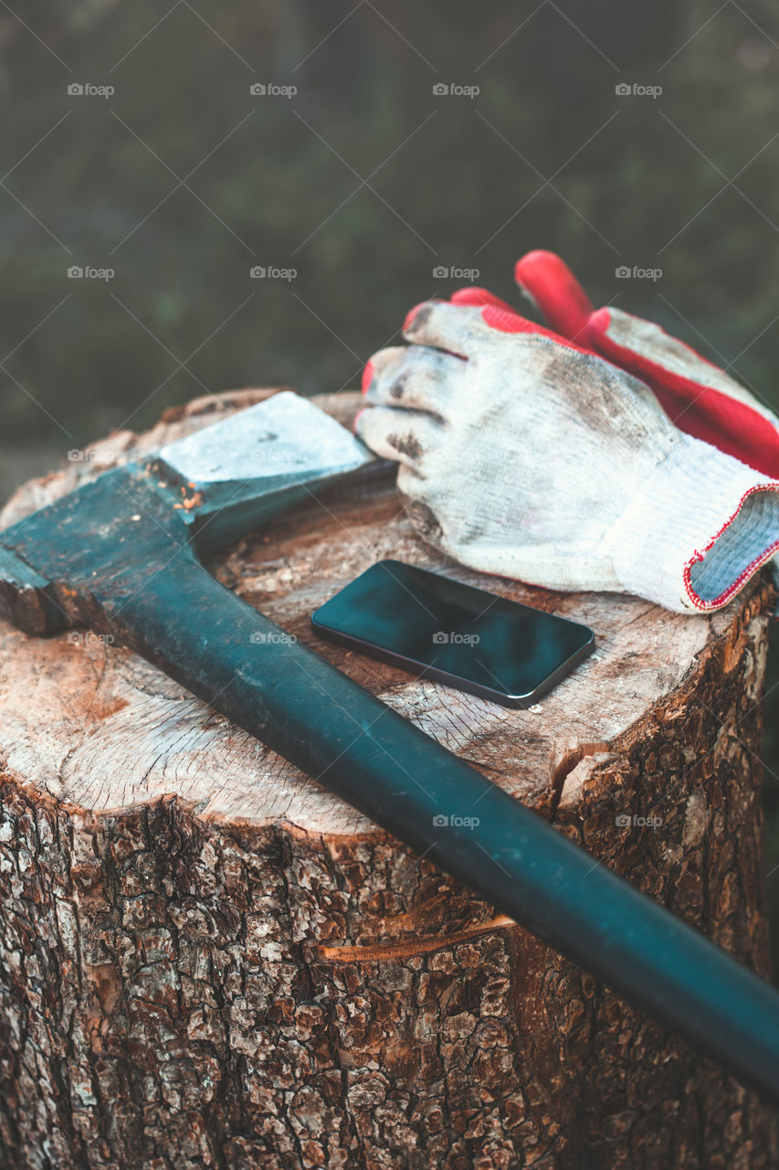 Mobile phone and tools, axe, work gloves on tree trunk