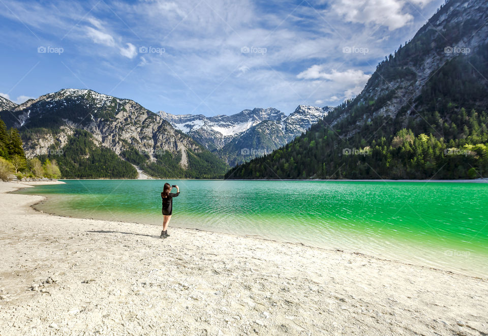 People from behind taking picture of beautiful scenic lake and mountains in Austria in spring time 