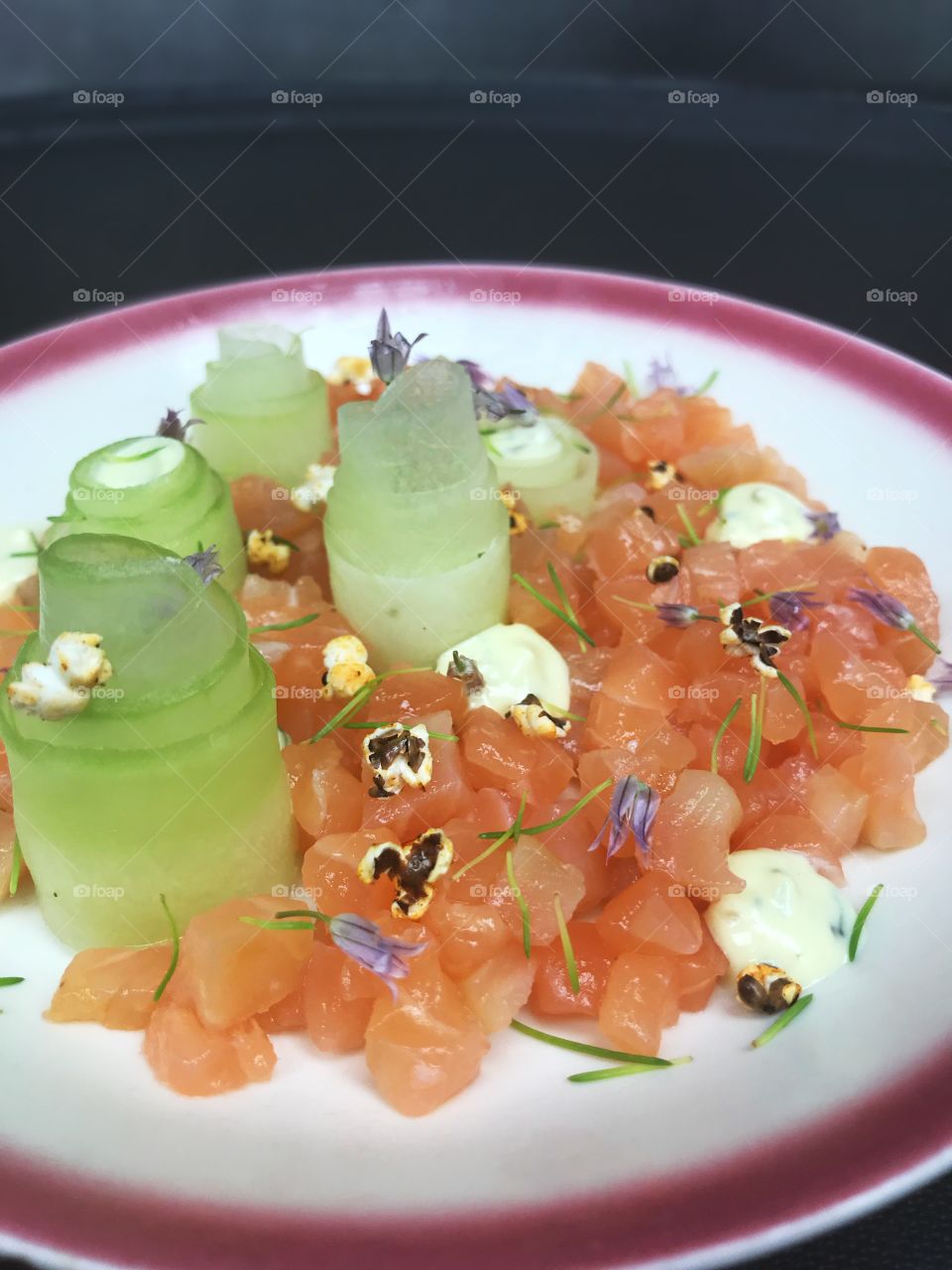 Salmon tartare with cucumber and flowers in a kitchen on a round plate