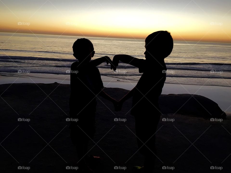 Brothers at the beach during sunset displaying a heart shape with their arms 