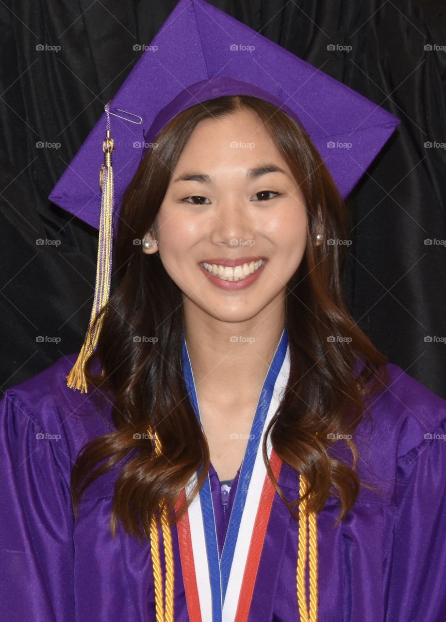 High school graduate wearing a purple cap and gown and honor cords, Chinese girl