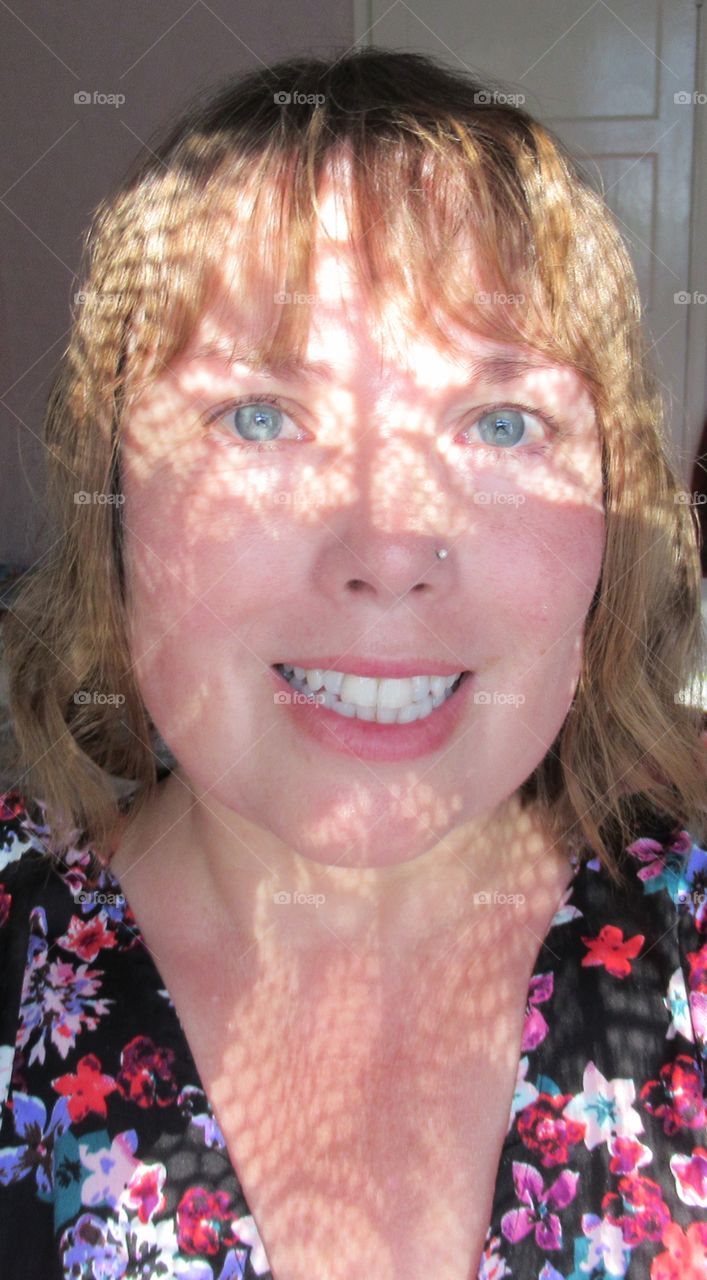 Portrait of a lady with sun shining through the window and the lace curtain making a pattern