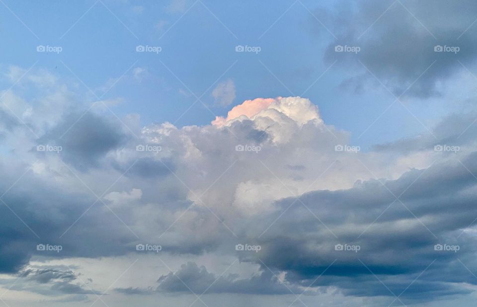 A pink cloud among grey and white clouds in the blue sky