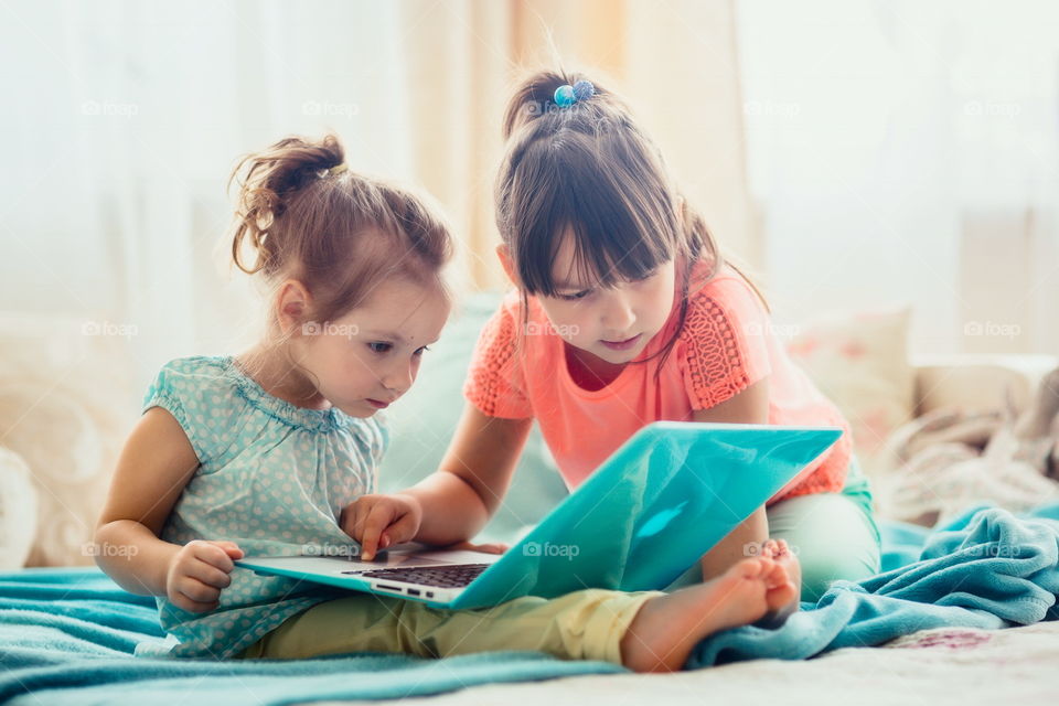 Little sisters with gadgets(laptop and tablet) in the bed.