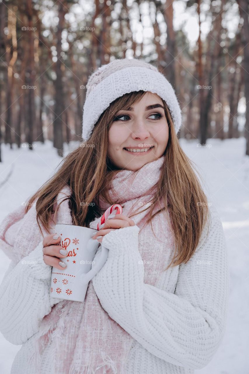 Happy girl hold cup of cacao with candy and smile in winter forest