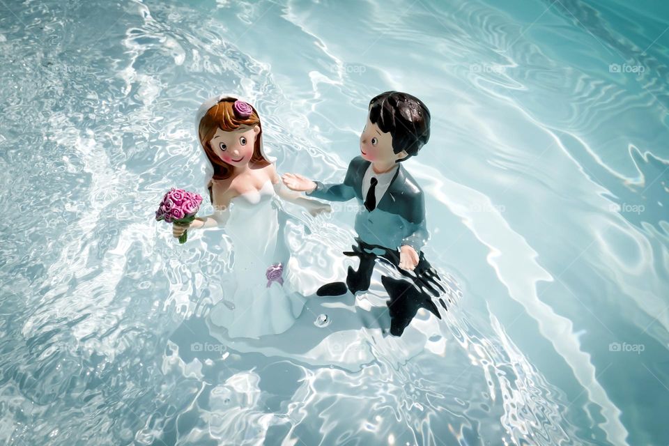 Two figurines of a married couple immersed in turquoise water, marriage celebration in water