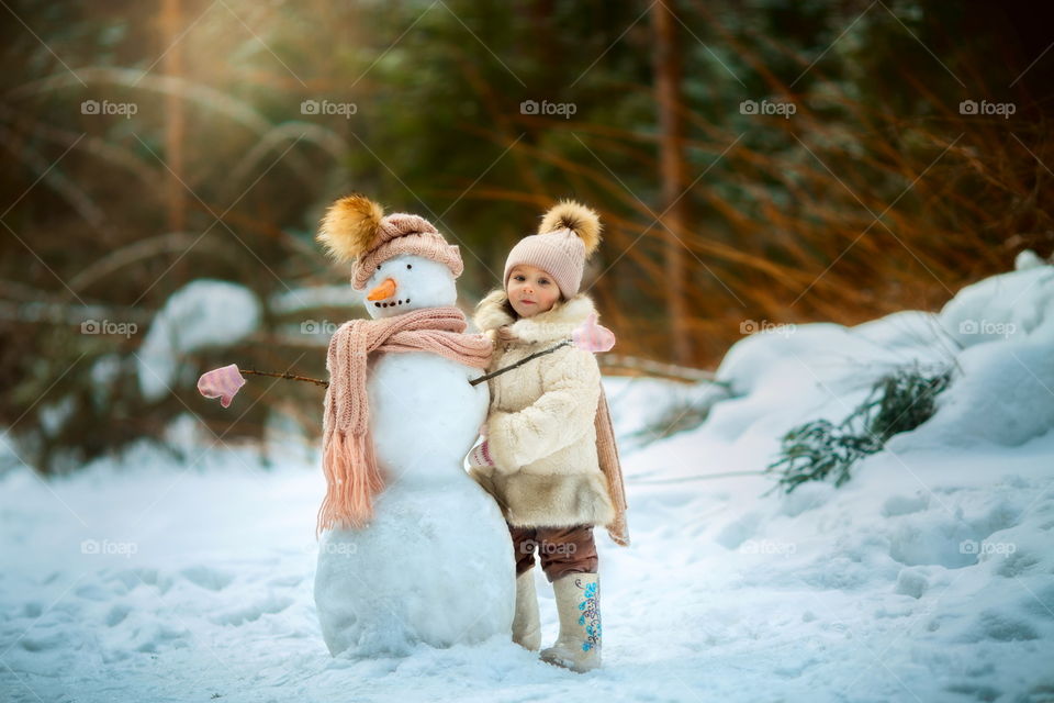 Little girl with snowman in winter park