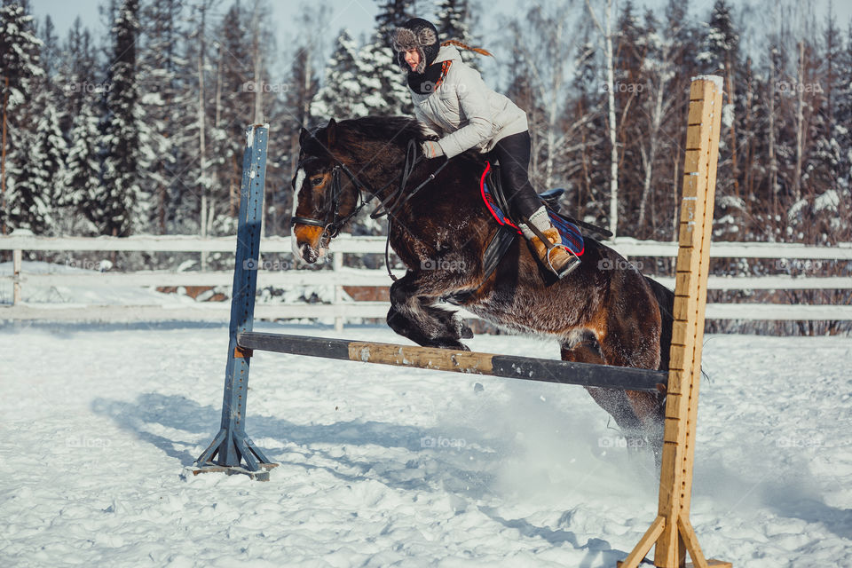 Teenage girl horseback jumping at cold winter day